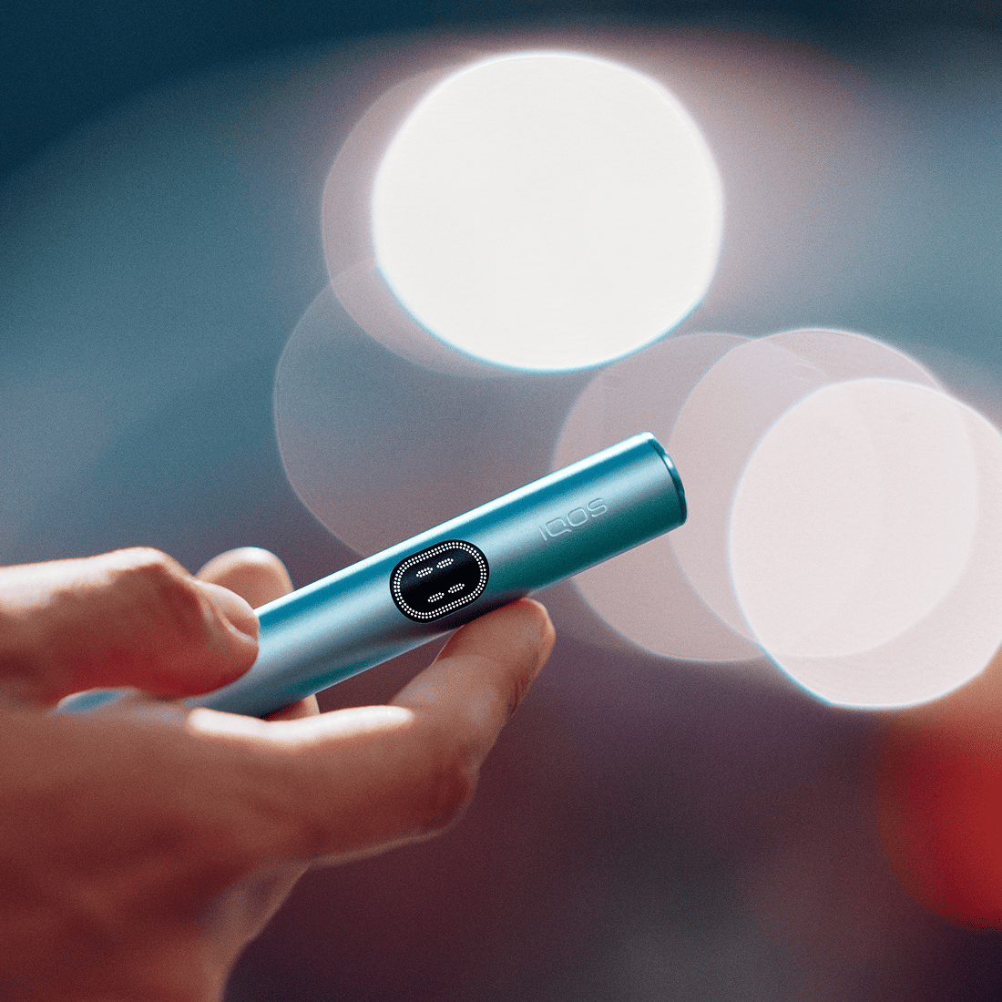 A person holding an IQOS ILUMA i color Breeze Blueholder on their hand